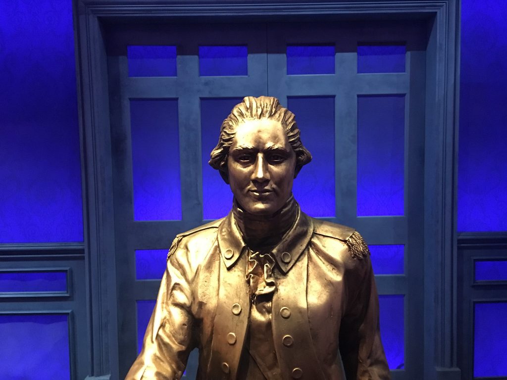 A golden statue of Alexander Hamilton against a blue background