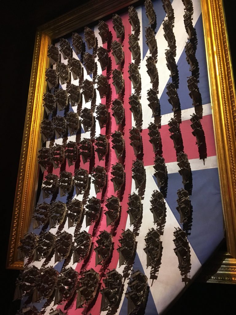 A union jack in a frame, with dozens of model British ships on top