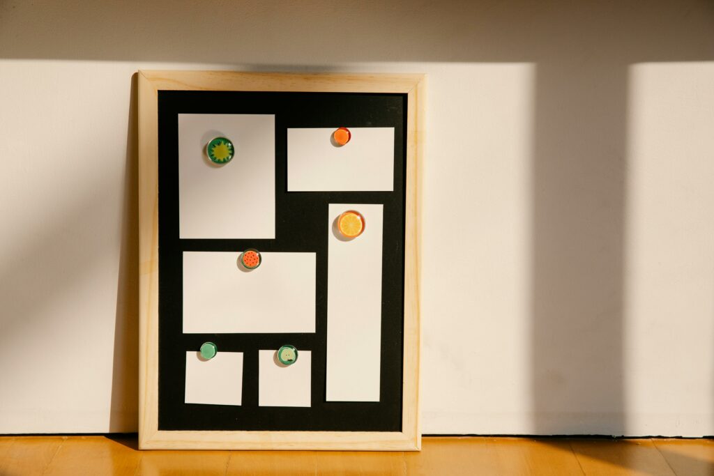 A photograph of a magnetic board with a wooden frame against a white wall. Pieces of white paper are held against the board by colorful magnets.