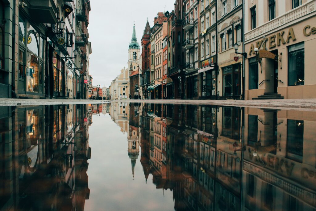 A photograph of a street that is possibly European, with buildings reflected in a puddle.