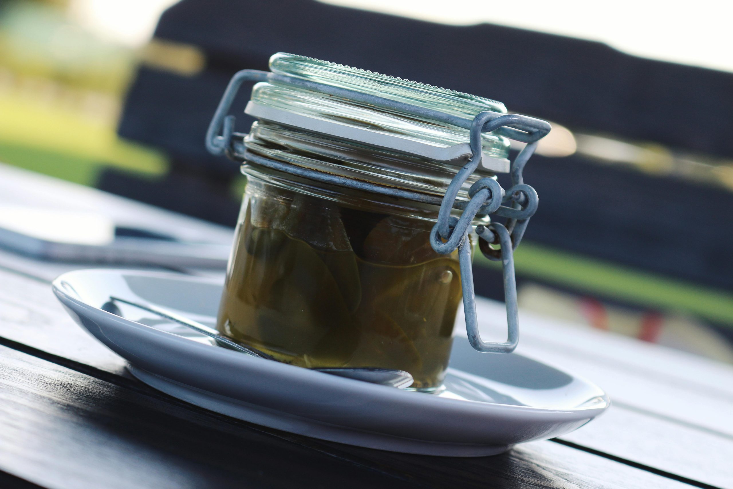 A photograph of a jar of pickles sitting on a small white plate. The photo is taken at an angle, so it looks like everything is sloping.