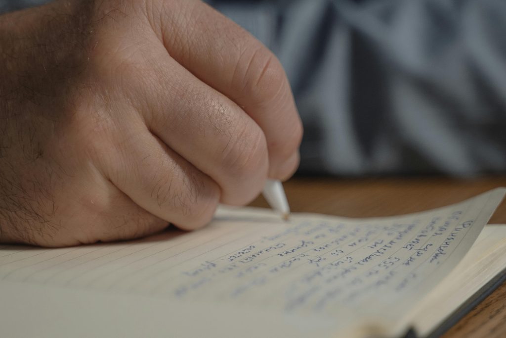 A photograph of someone's hand as they write with a pen on a piece of lined paper